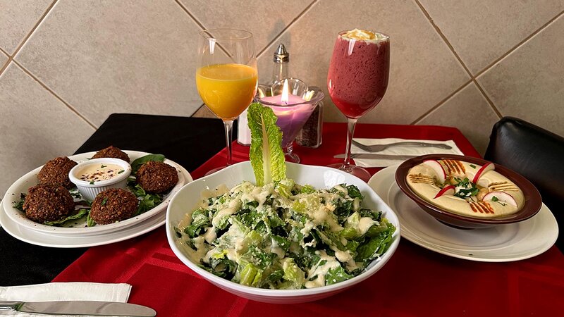 Table with plated falafel appetizer, hummus salad and drinks